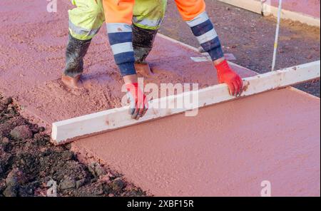 Constructeurs coulant et nivelant du béton prêt à l'emploi humide dans le coffrage lors de la construction d'un nouveau sentier Banque D'Images