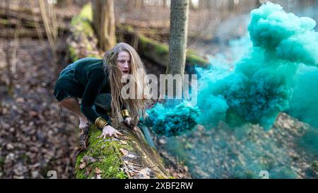 Une femme pose dans une forêt avec un panache de fumée bleue derrière elle. Faible profondeur de soudure Banque D'Images