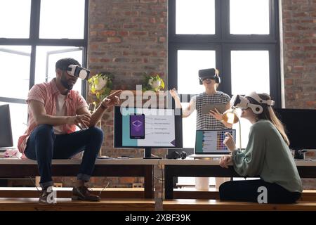 Femme d'affaires asiatique et jeune équipe diversifiée utilisant des casques VR dans le bureau moderne. Les grandes fenêtres et les murs de briques exposés créent un worksp ouvert et collaboratif Banque D'Images