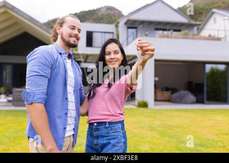 Jeune couple diversifié sourient tout en tenant les clés de la maison, achetant la première maison Banque D'Images