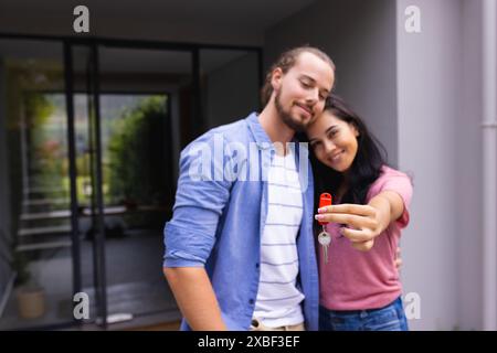 Jeune couple diversifié tient les clés de la maison ensemble, souriant, achetant la première maison Banque D'Images