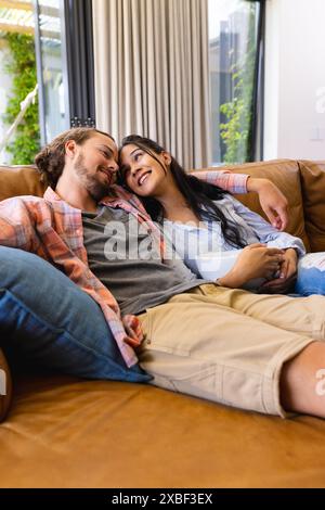 Une jeune femme biraciale et un jeune homme caucasien se détendent sur un canapé, souriant chaleureusement Banque D'Images