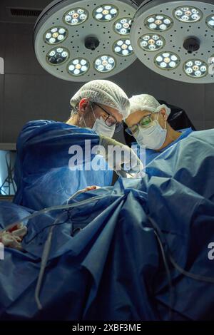 Deux chirurgiens pratiquant une chirurgie dans une salle d'opération sous de vives lumières Banque D'Images