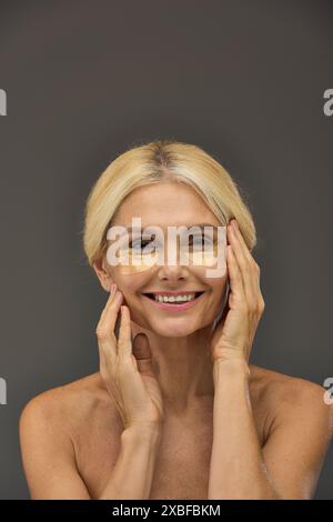 Belle femme mature avec des cheveux blonds avec des patchs pour les yeux sur un fond gris. Banque D'Images