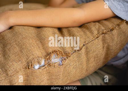 Un coussin de canapé brun déchiré en lin, avec un intérieur en fibre de polyester Banque D'Images