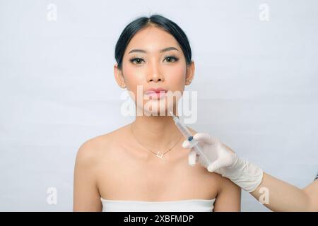 Femme asiatique avec des cheveux dans un pain subissant une injection de Botox pour resserrer la peau Banque D'Images