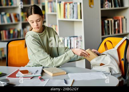 Une adolescente immergée dans ses études, assise à une table dans une bibliothèque, absorbée par le travail sur son ordinateur portable après l'école. Banque D'Images