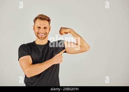 Un jeune homme athlétique en tenue active fléchissant ses biceps sur un fond gris, montrant la force et la détermination. Banque D'Images