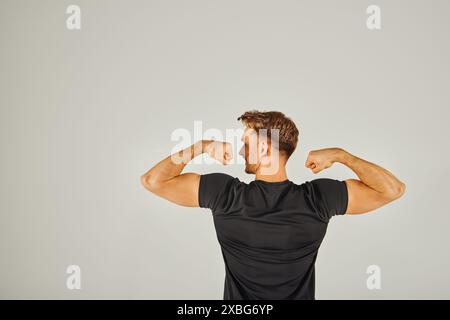 Un jeune athlétique fléchit ses muscles devant un fond blanc, mettant en valeur sa force et sa détermination. Banque D'Images