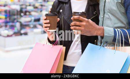 Deux amis dégustant un café tout en transportant des sacs à provisions au centre commercial Banque D'Images