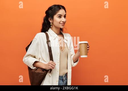 Une jeune femme indienne tient énergiquement une tasse de café sur un fond orange vif. Banque D'Images