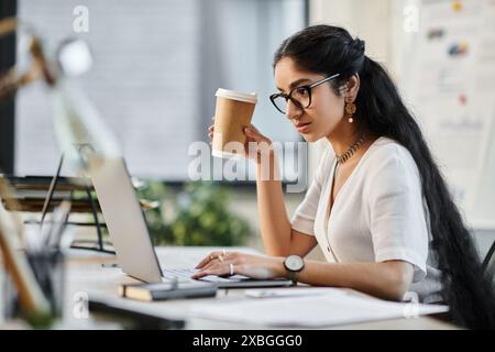 Une femme indienne, café à la main, est assise à un bureau dans un moment serein de contemplation. Banque D'Images
