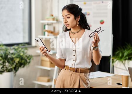 Jeune femme indienne activement engagée avec le téléphone dans le cadre de bureau. Banque D'Images