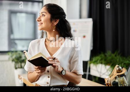 Jeune femme indienne engrossée dans la lecture d'un livre dans un cadre de bureau moderne. Banque D'Images