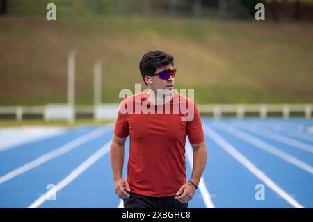 homme athlétique portant des lunettes de soleil et des écouteurs sans fil s'entraîne sur une piste athlétique. capture l'attention et le dévouement de l'athlète dans son engagement Banque D'Images