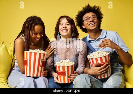 Un groupe diversifié d'amis dans une tenue élégante assis sur un canapé, tenant des seaux de pop-corn. Banque D'Images