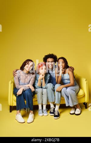 Un groupe diversifié de jeunes amis, y compris une personne non binaire, s'asseyent et discutent confortablement sur un canapé jaune vibrant dans un cadre de studio élégant. Banque D'Images