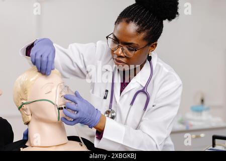 Une professionnelle médicale portant un manteau blanc et un stéthoscope pratique l'application d'un masque à oxygène sur un mannequin. Banque D'Images