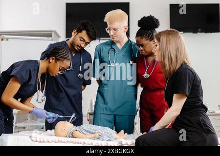 Quatre étudiants en médecine en gommage sont rassemblés autour d’un mannequin d’entraînement pour pratiquer les techniques de réanimation. Banque D'Images