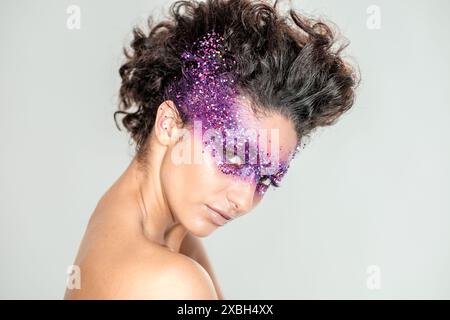 Le modèle beuatiful brnette mediterranean présente un look de maquillage étincelant violet d'une équipe créative dans un cadre de mode studio Banque D'Images