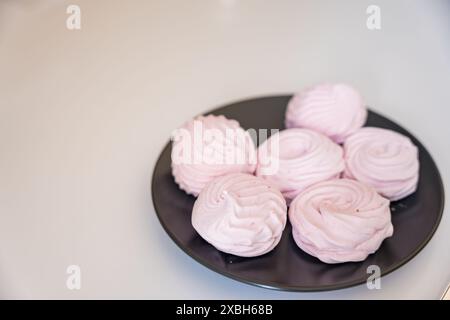 Gros plan de marshmallows meringués rose moelleux faits maison disposés sur une assiette sombre. Les délicats tourbillons et la texture douce font de ces friandises maison un del Banque D'Images