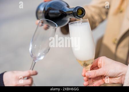 gros plan de deux mains de femmes tenant des verres de prosecco en cours de versement, capturant un moment de célébration plein de joie et d'élégance. parfait pour les thèmes Banque D'Images