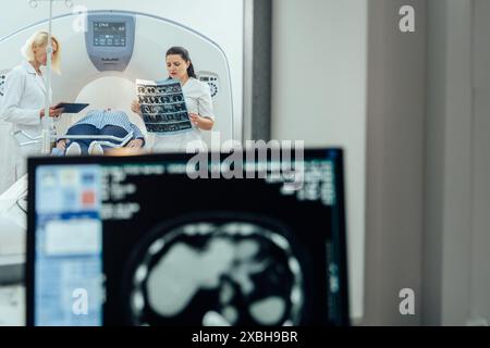 Médecin examinant les radiographies affichées dans la salle de contrôle IRM pendant qu'il était en arrière-plan, préparant le patient pour le test d'examen. Banque D'Images