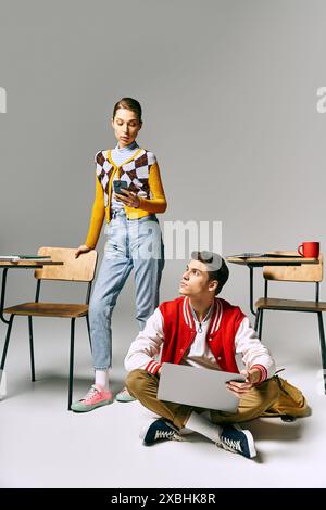 Un jeune homme et une jeune femme étudiants sont assis sur le sol, collaborant sur un ordinateur portable. Banque D'Images