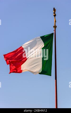 Le drapeau tricolore italien vole dans une brise modérée devant le monument Vittorio Emanuele II dans une Rome ensoleillée, en Italie Banque D'Images