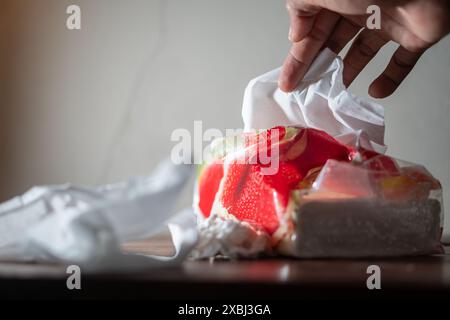 Main cherchant un mouchoir près d'une pastèque partiellement déballée sur une table. Banque D'Images