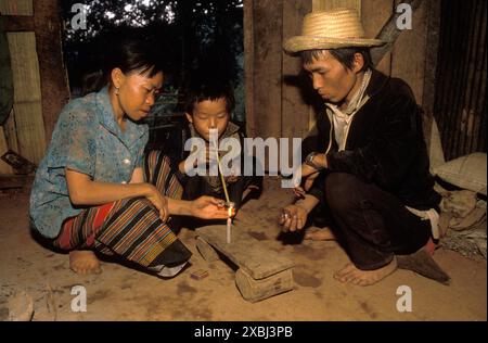 Village de Hmong, province de Chiang Rai, nord de la Thaïlande vers 1995. Les paysans de la tribu des collines à l'intérieur de leur maison, toute la famille est accro à l'opium, leur enfant fume de l'opium, le garçon a 8 ans. Banque D'Images