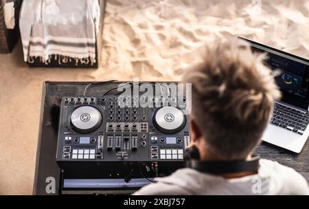 DJ mixant de la musique à la plage avec un ordinateur portable et un équipement professionnel. Le dj se produit lors d'un événement en plein air sur la plage de sable. Banque D'Images