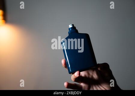 Une main tenant une bouteille de parfum rectangulaire bleu foncé avec une buse de pulvérisation sur un fond Uni. Banque D'Images