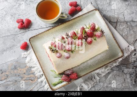 Gâteau roulé de Noël avec de la crème, de la confiture et des framboises fraîches gros plan sur l'assiette sur la table. Vue horizontale de dessus Banque D'Images