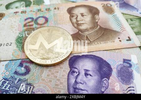 Gros plan sur une pièce de monnaie Monero dorée au-dessus d'une pile de billets de banque chinois Yuan. Banque D'Images