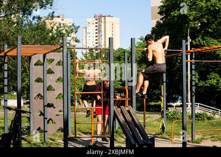 Un jeune homme effectue un muscle-up sur la barre horizontale, tandis que ses collègues s'entraînent sur d'autres appareils à Kiev (Kiev) Ukraine. Banque D'Images