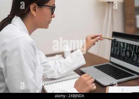 Diagnostic par rayons X : Focused Doctor in Glass analyse les images radiographiques affichées sur un ordinateur portable. Banque D'Images