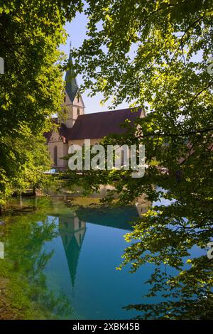 Allemagne, Blaubeuren - 20 août 2023 : L'église abbatiale se reflète dans les eaux bleues du Blautopf. Banque D'Images