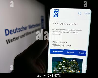 Personne tenant le téléphone portable avec la page Web du service météorologique allemand Deutscher Wetterdienst (DWD) avec logo. Concentrez-vous sur le centre de l'écran du téléphone. Banque D'Images