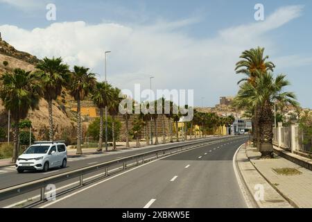 Almeria, Espagne - 25 mai 2023 : une camionnette blanche longe une route bordée de palmiers à Almeria, Espagne. La route est vide et il n'y a pas d'autres voitures Banque D'Images