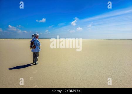 Femme âgée debout seule contre le soleil sur la plage, mer du Nord, composé Peter Ording, Schleswig Holstein, Allemagne Banque D'Images