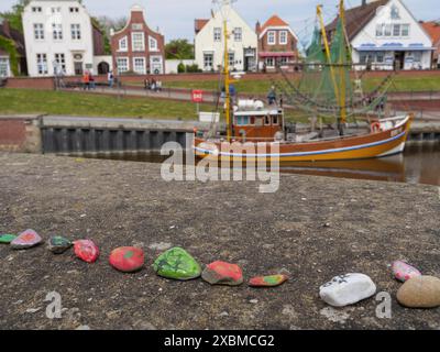 Une rangée de pierres peintes au bord de l'eau avec un bateau et des maisons colorées en arrière-plan, Greetsiel, Frise orientale, basse-Saxe, Allemagne Banque D'Images