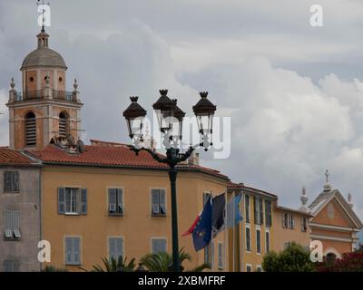 Une tour d'église et de vieilles lanternes devant des bâtiments historiques avec des drapeaux sous un ciel nuageux, ajaccio, corse, france Banque D'Images
