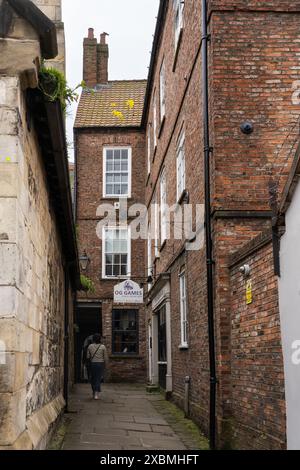 Une femme marchant vers le bas Whip-ma-Whop-ma-Gate - une rue de York, en Angleterre, connue pour sa courte longueur et son nom inhabituel, avec le No. 11/2 occupé par OG Games Banque D'Images