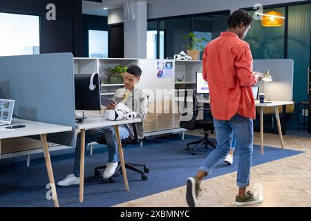 Un homme biracial est assis à un bureau, regardant son smartphone dans un bureau moderne Banque D'Images