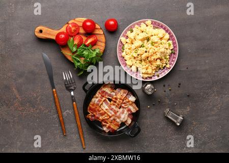 Savoureux oeufs brouillés, bacon et tomates sur fond gris Banque D'Images