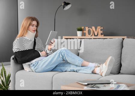 Jeune femme blessée après un accident en utilisant un ordinateur tablette sur le canapé à la maison Banque D'Images