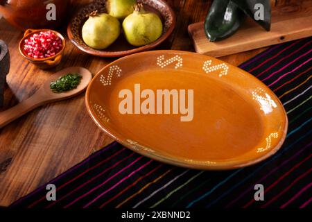 Fond de cuisine mexicaine. Assiette traditionnelle en argile vide sur une table rustique en bois avec des ingrédients de base pour préparer des chiles en nogada, un d mexicain typique Banque D'Images