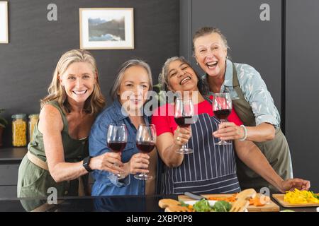 Groupe diversifié de femmes matures appréciant le vin et préparant la nourriture ensemble dans la cuisine Banque D'Images