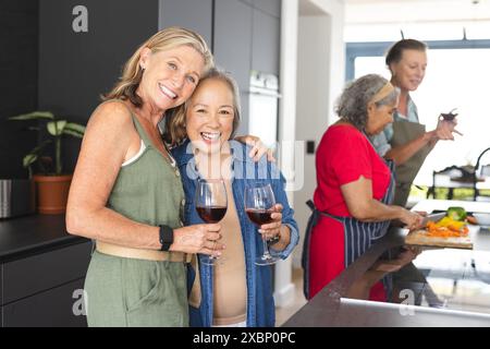 Groupe diversifié de femmes matures appréciant le vin et préparant la nourriture ensemble dans la cuisine Banque D'Images